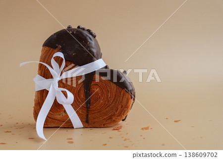 Tied bow ribbon on Delicious fresh croissant topped with Dark chocolate flavor Ganache. Creation unique heart shape bakery. Puff pastry holiday love gift present idea Valentine's day 138609702