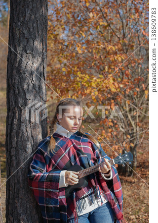 Blonde woman playing guitar ukulele outdoors in autumn forest. Concept of sound therapy, mental health and wellness rituals. Calmness tranquility audio-sensory practices. Aura farming Blonde woman playing guitar ukulele outdoors in autumn forest. Concept of sound therapy, mental health and wellness rituals. Calmness tranquility audio-sensory practices. Aura farming 138609783