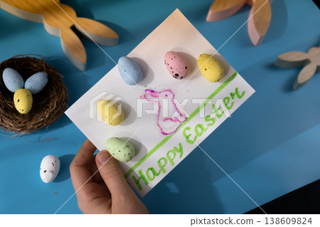 Person holding handmade greeting card with message HAPPY EASTER written in beautiful handwriting. Gesture shows excitement and joy for the upcoming event. Springtime holiday gift present zero cost Person holding handmade greeting card with message HAPPY EASTER written in beautiful handwriting. Gesture shows excitement and joy for the upcoming event. Springtime holiday gift present zero cost 138609824
