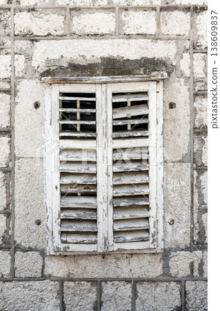 Weathered white wooden shutters set in an old stone wall 138609837