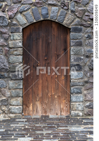 A rustic arched wooden door recessed into a weathered stone wall A rustic arched wooden door recessed into a weathered stone wall 138609849