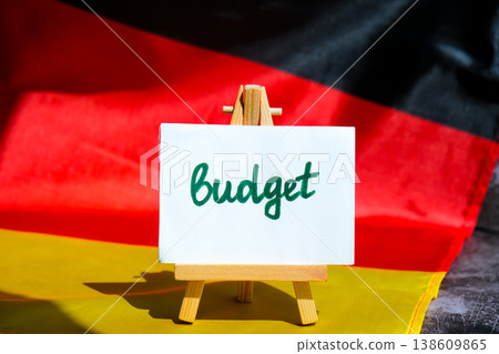 Paper note with words BUDGET on National symbol of Germany. German wave silky flag background. Economy federal annual finance planning Paper note with words BUDGET on National symbol of Germany. German wave silky flag background. Economy federal annual finance planning 138609865