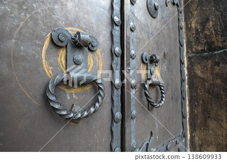 Close-up of two twisted metal ring knockers on a dark, weathered metal door with rivet details 138609933