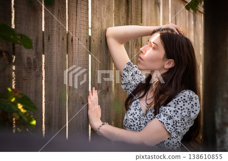 Young woman by wooden fence in warm sunlight Young woman by wooden fence in warm sunlight 138610855