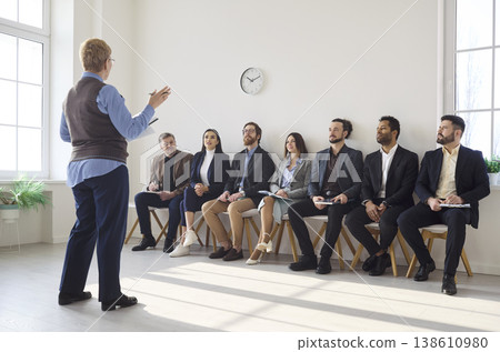 Business coach conducting team workshop with seated group in modern bright office 138610980