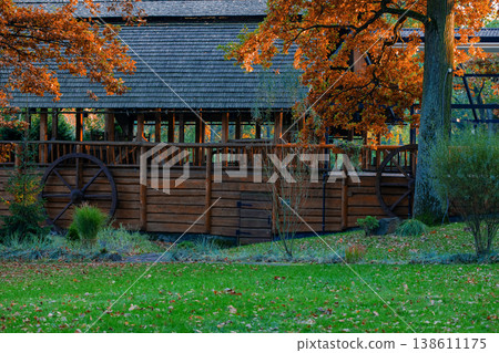 A rustic wooden watermill with a large wheel and gray shingled roof surrounded by autumn foliage and green grass A rustic wooden watermill with a large wheel and gray shingled roof surrounded by autumn foliage and green grass 138611175