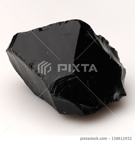 Large Piece of Polished Black Obsidian Volcanic Glass with Sharp Edges and Smooth Reflective Surface on White Background. 138612052