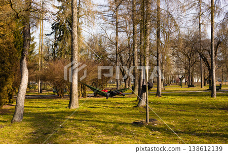 Peaceful park scene with hammocks stretched between trees, green grass and soft sunlight creating relaxing atmosphere, outdoor leisure  138612139