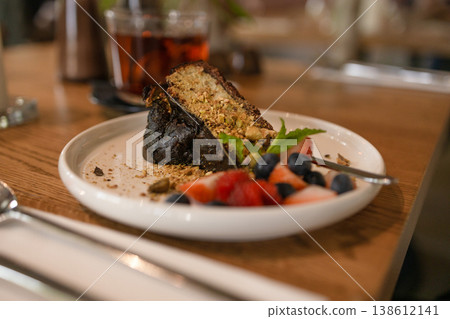Slice of chocolate cake served with fresh berries and tea on wooden table in cozy cafe environment with soft natural light. 138612141