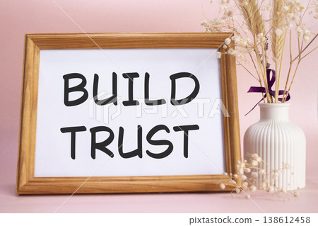Build trust symbol. Concept words Build trust on beautiful wooden picture frame. Beautiful pink background with flower vase. Business and Build trust concept. Copy space. Build trust symbol. Concept words Build trust on beautiful wooden picture frame. Beautiful pink background with flower vase. Business and Build trust concept. Copy space. 138612458