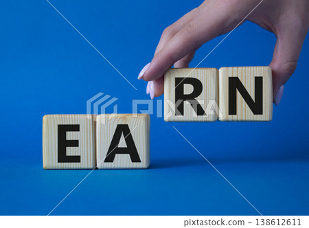 Earn symbol. Concept word Earn on wooden cubes. Businessman hand. Beautiful blue background. Business and Earn concept. Copy space. Earn symbol. Concept word Earn on wooden cubes. Businessman hand. Beautiful blue background. Business and Earn concept. Copy space. 138612611