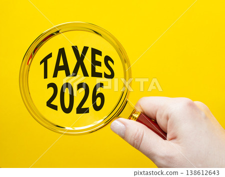 TAXES 2026 symbol. Magnifying Glass with words TAXES 2026. Businessman hand. Beautiful yellow background. Business and TAXES 2026 concept. Copy space. TAXES 2026 symbol. Magnifying Glass with words TAXES 2026. Businessman hand. Beautiful yellow background. Business and TAXES 2026 concept. Copy space. 138612643