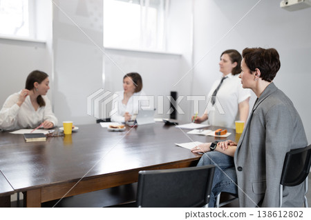 Women colleagues in light filled meeting room sitting at table with notebooks and orange juice, talking. Meeting, colleagues, talking, juice, business, teamwork. Women colleagues in light filled meeting room sitting at table with notebooks and orange juice, talking. Meeting, colleagues, talking, juice, business, teamwork. 138612802