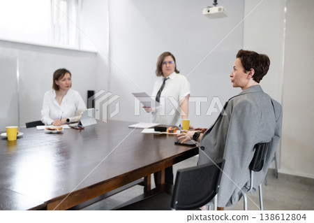 Professional women standing and talking with colleagues at wooden office table in modern workplace. Talking, standing, table, women, office, professional. Professional women standing and talking with colleagues at wooden office table in modern workplace. Talking, standing, table, women, office, professional. 138612804