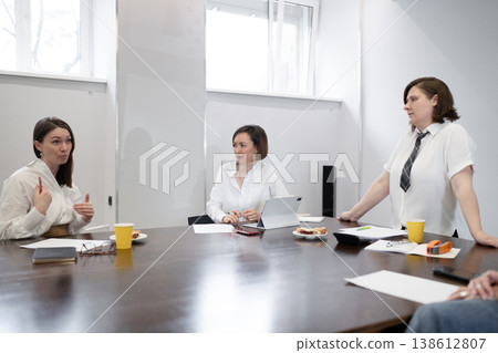 Female business partners seated and communicating at meeting table during group breakfast in office. Partners, breakfast, group, meeting, communicating, office. Female business partners seated and communicating at meeting table during group breakfast in office. Partners, breakfast, group, meeting, communicating, office. 138612807