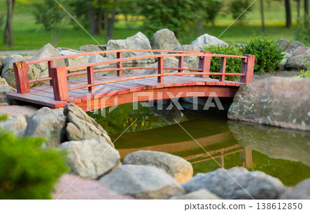 small red wooden bridge over a pond in a serene garden with large rocks and greenery 138612850
