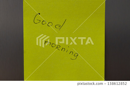 A bright yellow sticky note with a handwritten good morning message on a dark background 138612852