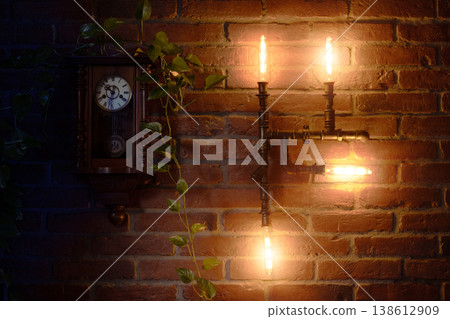 Steampunk vintage clock and industrial style lamp on a brick wall with green plant warm low key illumination lamp Steampunk vintage clock and industrial style lamp on a brick wall with green plant warm low key illumination lamp 138612909