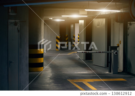 A dimly lit parking garage with a barrier arm and yellow markings on the floor and pillars 138612912