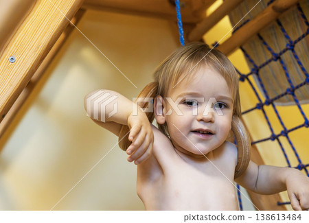 Adorable toddler with pigtails smiling while gripping gym rings near climbing net Adorable toddler with pigtails smiling while gripping gym rings near climbing net 138613484