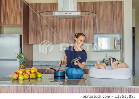 Mother talking to baby lying in cozy lounger on kitchen table while cooking at home. Caring mom interacting with infant during daily routine. Parenting, multitasking and family life concept Mother talking to baby lying in cozy lounger on kitchen table while cooking at home. Caring mom interacting with infant during daily routine. Parenting, multitasking and family life concept 138613855