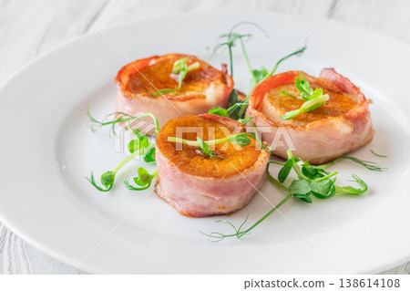 King oyster mushrooms wrapped in crispy bacon served as elegant gourmet appetizer on white plate 138614108