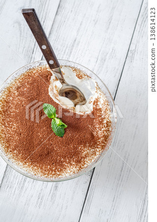 Close up tiramisu dessert in glass bowl with spoon revealing creamy layers 138614123