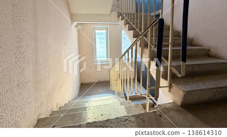 Apartment building stairwell with concrete stairs going down, metal railings and sunlight through window. Apartment building stairwell with concrete stairs going down, metal railings and sunlight through window. 138614310