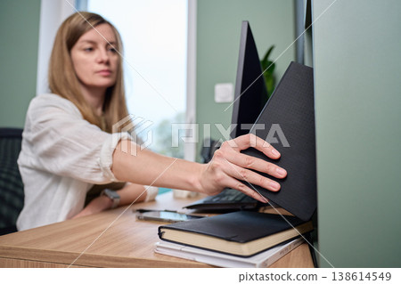 Woman placing notebook on shelf next to desk with monitor and smartphone Woman placing notebook on shelf next to desk with monitor and smartphone 138614549