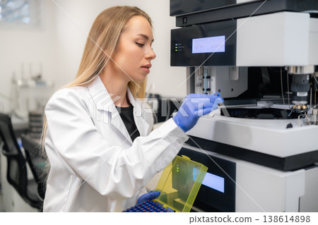 Laboratory technician inserting HPLC vials into advanced analytical equipment for testing in a pharmaceutical lab. Laboratory technician inserting HPLC vials into advanced analytical equipment for testing in a pharmaceutical lab. 138614898