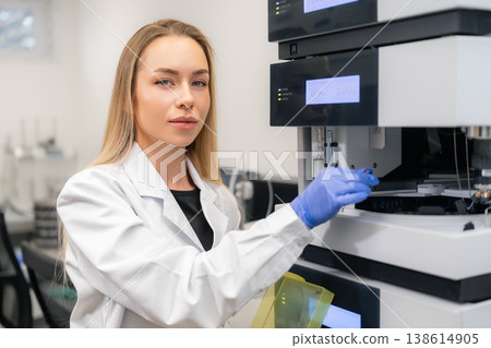 Technician calibrating advanced HPLC chromatographic system at modern pharmaceutical lab workstation. Clean environment with digital displays and analytical instruments visible in the background. 138614905