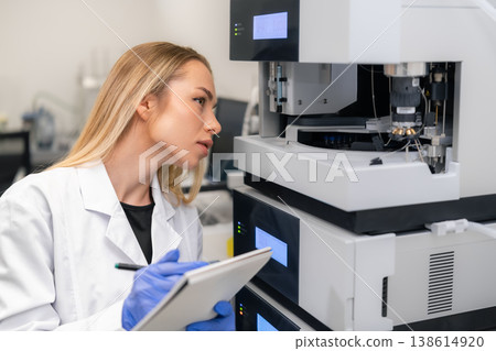 Scientist examining advanced chromatographic equipment HPLC while recording observations in a laboratory environment. 138614920