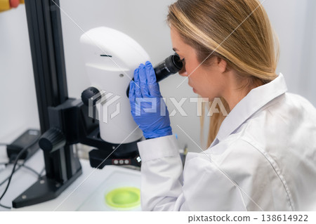 Laboratory technician analyzing biological specimens using a digital microscope at clinical workstation. The clean setting includes precision equipment and visible sample trays. Laboratory technician analyzing biological specimens using a digital microscope at clinical workstation. The clean setting includes precision equipment and visible sample trays. 138614922