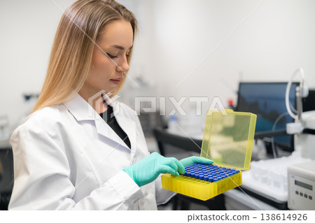 Scientist checks HPLC vials in yellow storage box at pharmaceutical laboratory workstation 138614926