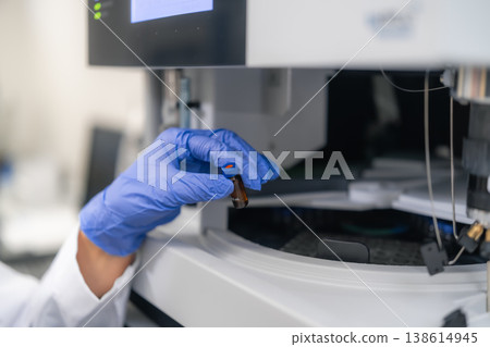 Conducting precise sample analysis using a brown vial within an advanced HPLC system. The workspace features modern equipment and digital displays, reflecting a systematic workflow. 138614945