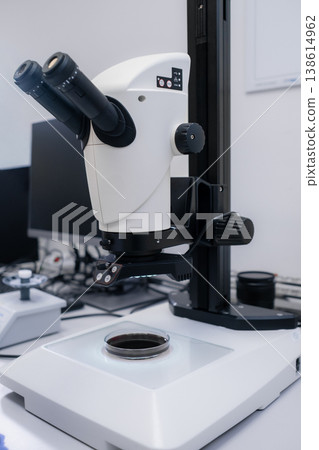 Advanced digital microscope positioned over a glass slide containing biological specimen at research workstation. Advanced digital microscope positioned over a glass slide containing biological specimen at research workstation. 138614962
