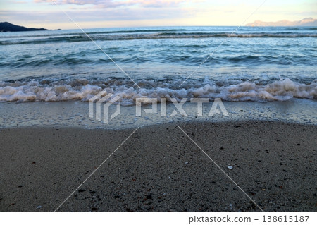 Close-up of a wave crashing onto the shore, clear water, foam bubbles and dark sand under a cloudy sky 138615187