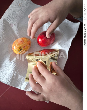A child wraps an Easter egg in shiny gold foil to paint it gold. A child wraps an Easter egg in shiny gold foil to paint it gold. 138615456