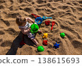 Toddler sitting on sandy beach playing with plastic bucket shovel and sand molds. Outdoor beach photography. Childhood and summer vacation concept. Design for poster, banner, postcard. Top view shot 138615693