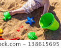 Toddler legs with green bucket and colorful sand molds scattered on beach sand. Outdoor beach photography. Childhood play and summer vacation concept. Close up shot 138615695