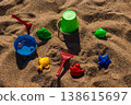 Overturned plastic bucket with shovel rake and sand molds arranged on beach sand. Flat lay beach composition. Summer vacation and children play concept Flat lay composition 138615697
