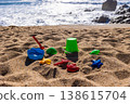 Plastic bucket with beach tools and molds placed on sand with sea and rocks in background. Outdoor beach photography. Summer vacation and seaside recreation concept. Wide angle shot 138615704