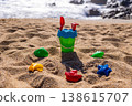 Children plastic bucket with shovel and rake on sandy beach near sea with toy molds around. Outdoor beach photography. Summer vacation and seaside play concept Eye level shot 138615707