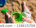 Toddler hands holding green bucket with sand pouring into it on beach. Outdoor beach photography. Childhood activity and summer vacation concept. Design for poster, banner, postcard. Top view shot 138615708
