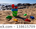 Plastic bucket with shovel and rake on sand with colorful toy molds on beach and sea background. Outdoor beach photography. Summer vacation and travel concept. Low angle shot 138615709