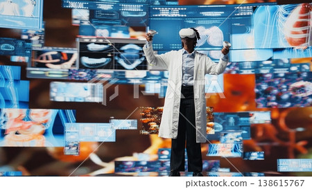 Virtual reality technology used by healthcare expert looking at CT scans, MRI data, and lab analytics on videowall. Scientist in medical research lab reading health data with VR goggles gear, camera A Virtual reality technology used by healthcare expert looking at CT scans, MRI data, and lab analytics on videowall. Scientist in medical research lab reading health data with VR goggles gear, camera A 138615767