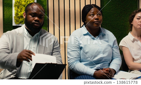 Anxious diverse job seekers awaiting job interview discussion with manager, showcasing anticipation in office hallway. People preparing with information for the recruitment process. 138615778