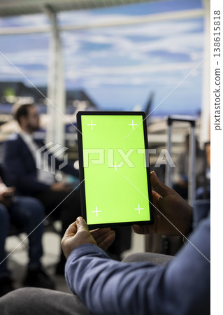 Vertical chroma key tablet in international airport terminal with diverse passengers relaxing in waiting lounge. Travelers with suitcases checking passports and plane tickets before journey. 138615818