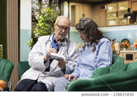 Doctor performs in-home exam giving prescribed medicine to old woman, explaining pills dosage as part of private healthcare services. Home care services emphasizes preventive checkup for safety. 138615830