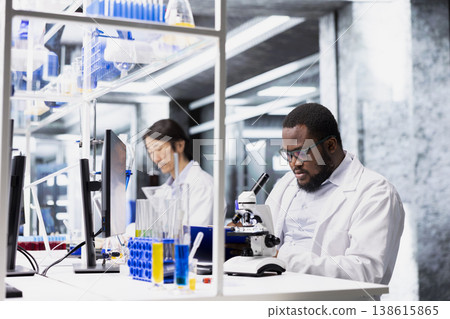 Clinical microbiologist in lab using scientific microscope for cellular analysis, researching molecular data. Research facility professional using optical device gear to examine medical samples Clinical microbiologist in lab using scientific microscope for cellular analysis, researching molecular data. Research facility professional using optical device gear to examine medical samples 138615865